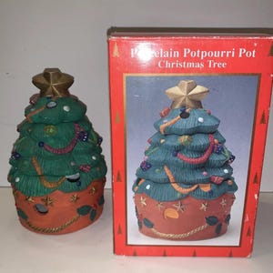 May include: A ceramic Christmas tree potpourri holder with a red base, green tree, and gold star on top. The box reads "Porcelain Potpourri Pot Christmas Tree".