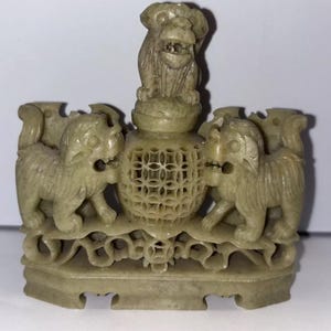 May include: A carved jade stone sculpture of a Chinese foo dog with a smaller foo dog on top. The sculpture is intricately detailed and has a green and white colour scheme.