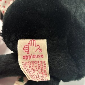 May include: A black plush toy with a tag that reads "applause". The tag has a hand logo and additional text. The toy has a white and red polka dot pattern on the top.