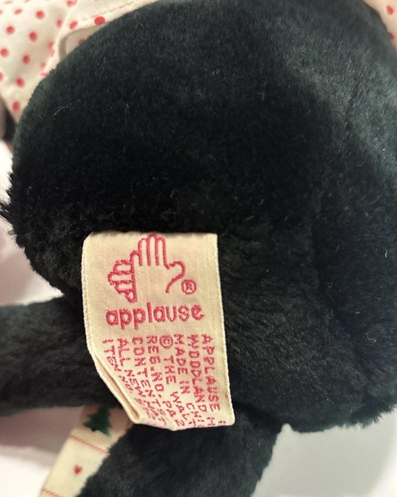 May include: A black plush toy with a tag that reads "applause". The tag has a hand logo and additional text. The toy has a white and red polka dot pattern on the top.
