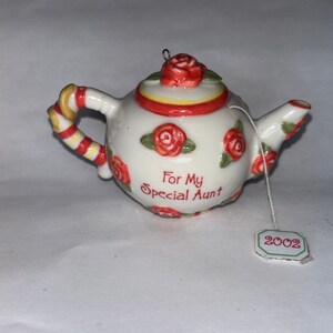 May include: A white ceramic teapot ornament decorated with red roses and green leaves. The handle is striped with red, yellow, and white. The text "For My Special Aunt" is on the front. A tag reads "2002".