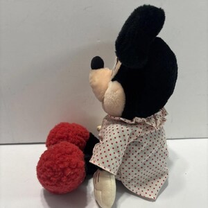 May include: A Minnie Mouse soft toy, with black ears, a black nose, and a cream-coloured face. She is dressed in a white dress with red polka dots and red, textured shoes. A classic Disney character.