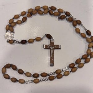 May include: A rosary with wooden beads in shades of brown and a silver crucifix. The cross features a silver figure of Jesus. The rosary also includes a silver medallion with religious symbols.