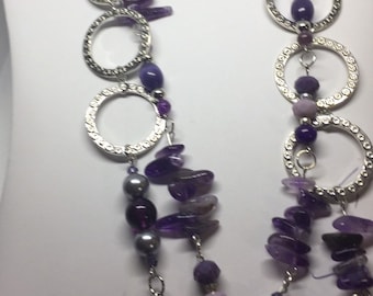 Könnte beinhalten: Eine silberne Kettenkette mit mehreren silbernen Kreisen und violetten Amethyststeinen. Die Kette hat einen mehrschichtigen Look mit verschiedenen Größen von Amethyststeinen.