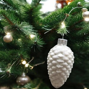 May include: White pine cone shaped Christmas ornament with a glittery finish hanging on a green Christmas tree.