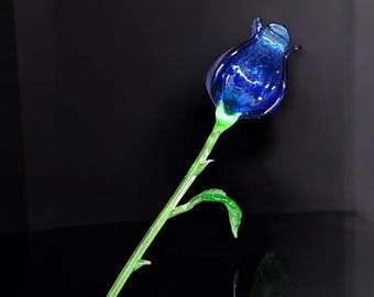 May include: A single blue glass rose with a green stem and leaves. The rose is made of glass and has a shiny finish.