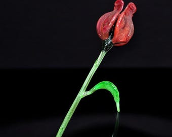 May include: A single glass flower with a red and pink bud and a green stem.