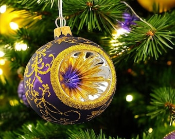 May include: A purple Christmas ornament with gold glitter and a gold and purple swirl design. The ornament has a clear, round window that reveals a gold and purple swirl design.