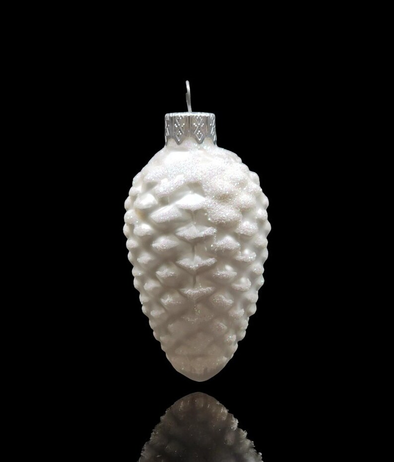 May include: White glass Christmas ornament shaped like a pine cone with a glittery finish.