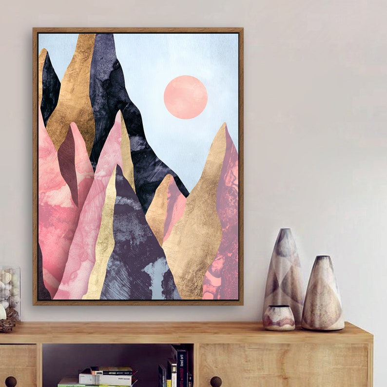 May include: Abstract art print featuring a mountain range with pink, gold, and blue hues. The mountains are layered and textured, creating a sense of depth. A pink circle is in the sky above the mountains.