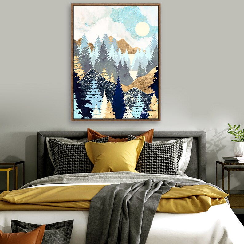 May include: A framed abstract painting of a forest scene with blue, gold, and white colors. The painting depicts a forest with trees and mountains in the background. The sky is a light blue with white clouds and a sun.