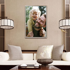 Puede incluir: Una fotograf&iacute;a enmarcada de un hombre sonriente que lleva a un ni&ntilde;o sobre sus hombros. La foto se muestra en una pared beige sobre un sof&aacute; blanco con cojines grises. El marco es plateado.