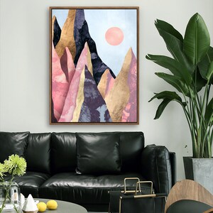 May include: Abstract art print featuring a mountain range with pink, gold, and purple hues. The mountains are set against a light blue sky with a pink sun.