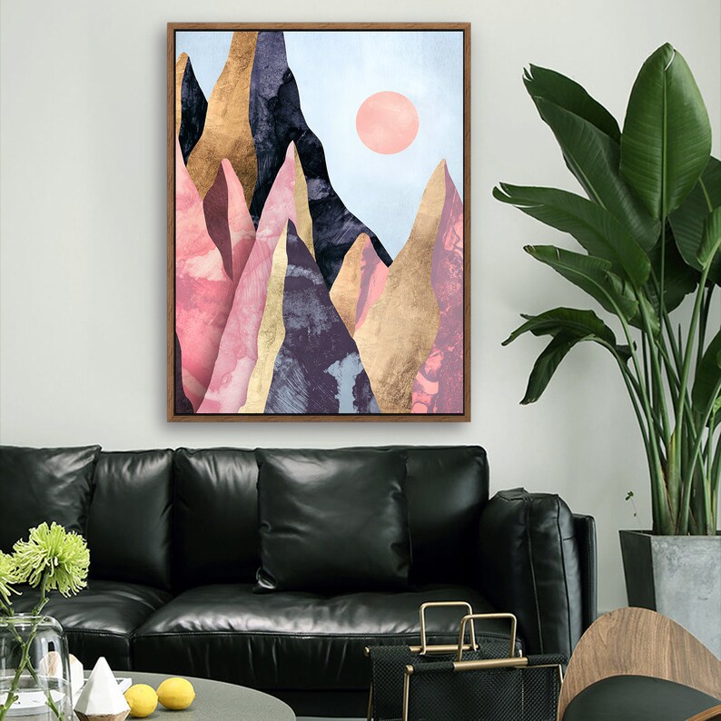May include: Abstract art print featuring a mountain range with pink, gold, and purple hues. The mountains are set against a light blue sky with a pink sun.