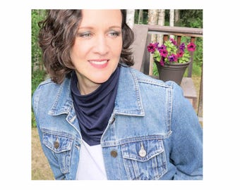 May include: A woman wearing a navy blue neck warmer under a denim jacket. She has short, curly brown hair and is looking to the right.