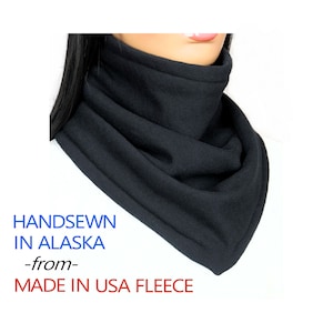 May include: Black fleece neck warmer, handmade in Alaska.  The neck warmer is folded and has a seam around the edge.  The text "HANDSEWN IN ALASKA -from- MADE IN USA FLEECE" is printed below the neck warmer.