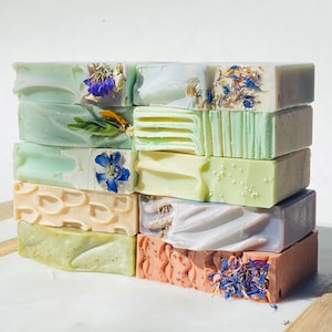 May include: A stack of ten rectangular bars of soap with various colors and patterns. The soap bars are decorated with dried flowers and herbs.