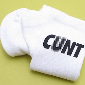 May include: White ankle socks with the word "CUNT" printed in black letters.