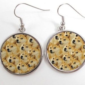 May include: Silver dangle earrings with a round, white, silver-rimmed charm featuring a repeating pattern of Shiba Inu dog faces.