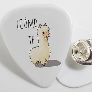 May include: White guitar pick with a cartoon alpaca and the text "¡cómo te" in black.