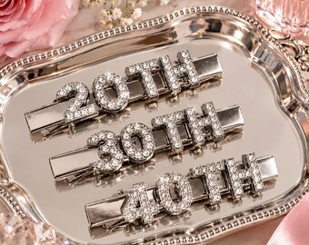May include: Three silver-toned metal hair clips, each featuring rhinestone-encrusted lettering. The clips display the text 20TH, 30TH, and 40TH respectively, with clear crystals set into the surface of each number and letter character.