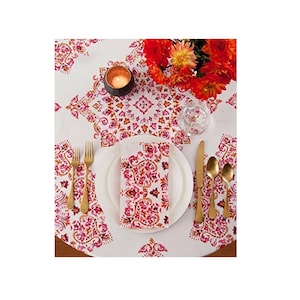 Peut inclure: Une nappe blanche avec un motif floral rose et orange. Une mise en place avec des couverts en or, une assiette blanche et une serviette en tissu rose et orange est sur la table.