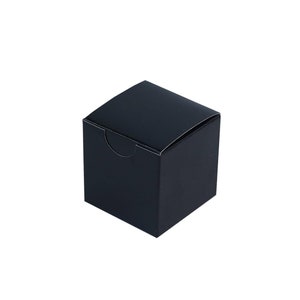 Könnte beinhalten: Eine schwarze quadratische Geschenkbox mit schlichtem Design. Die Box ist aus Pappe und hat eine glatte Oberfläche.