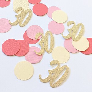 Può includere: Confetti dorati con glitter con il numero 30 su ogni pezzo. Il confetti è sparso su uno sfondo bianco con cerchi rosa e crema.