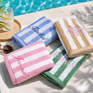 Peut inclure: Quatre serviettes rectangulaires pliées à rayures verticales bleues, beiges, roses et vertes. Chaque serviette est brodée d'un nom ou d'un monogramme en écriture cursive, incluant les prénoms Rachel, Jenna, Emma et le monogramme NLE avec un nœud.