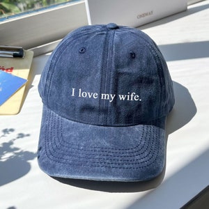 May include: A dark blue denim baseball cap with white embroidery that reads "I love my wife."
