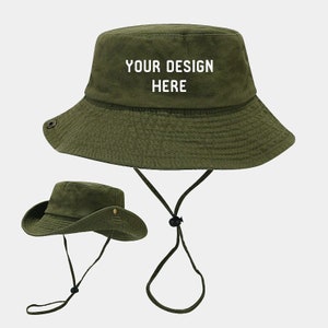 Peut inclure: Un chapeau bob vert avec une sangle réglable blanche et le texte "YOUR DESIGN HERE" brodé sur le devant.