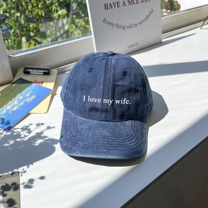 May include: A dark blue denim baseball cap with white embroidery that reads "I love my wife."