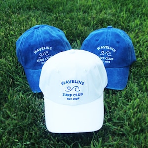 May include: Three baseball caps, two blue and one white, with the logo "Wavelline Surf Club Est. 2004" embroidered in blue on each cap.
