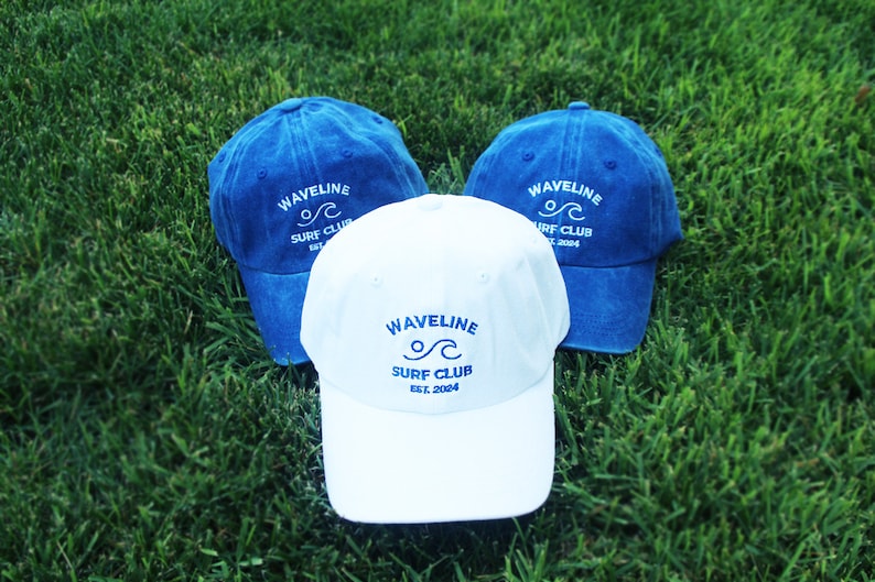May include: Three baseball caps, two blue and one white, with the logo "Wavelline Surf Club Est. 2004" embroidered in blue on each cap.
