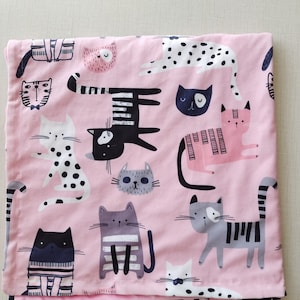 May include: Pink fabric with a repeating pattern of black and white cats. The cats are in various poses and have different facial expressions.