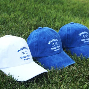 May include: Two baseball caps with the text "Wavelink Surf Club Est. 2004" embroidered on the front. One cap is white with blue embroidery and the other is blue with white embroidery.