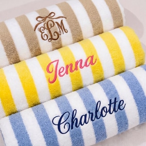 Könnte beinhalten: Drei Plüschhandtücher mit weißen und farbigen Streifen. Das obere Handtuch ist beige mit einem braunen gestickten Monogramm ELM. Das mittlere Handtuch ist gelb mit dem Namen Jenna in Pink. Das untere Handtuch ist hellblau mit dem Namen Charlotte in Marineblau.