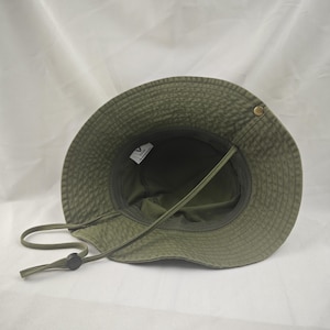 May include: Green bucket hat with a brown chin strap and a black toggle. The hat has a label inside that says "VINTAGE".