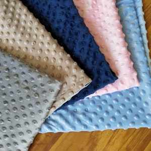 May include: Five fabric swatches in different colors: light gray, beige, navy blue, light pink, and light blue. The fabric has a textured, raised dot pattern.
