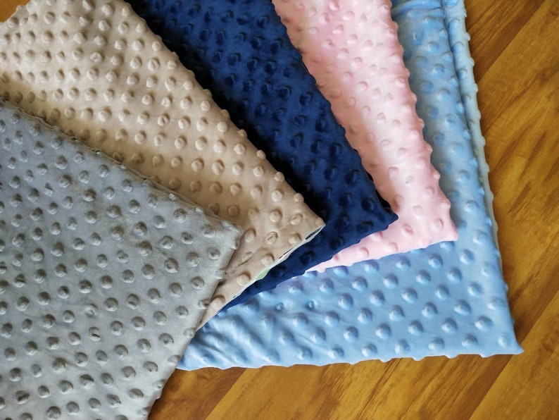 May include: Five fabric swatches in different colors: light gray, beige, navy blue, light pink, and light blue. The fabric has a textured, raised dot pattern.