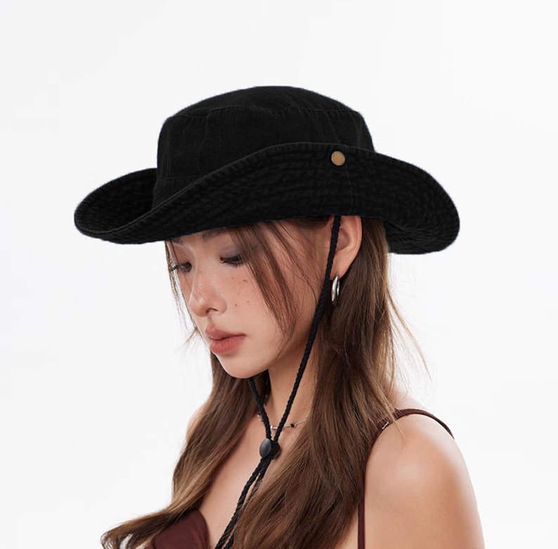 May include: A black wide-brimmed hat with a chin strap. The hat is made of a soft, textured fabric.