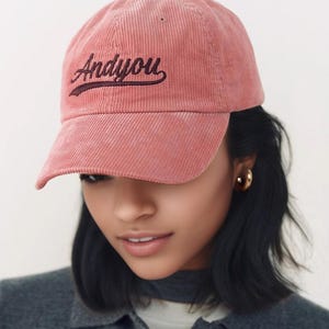 Puede incluir: Una gorra de b&eacute;isbol de pana rosa con el texto "Andy You" bordado en marr&oacute;n oscuro en la parte delantera.