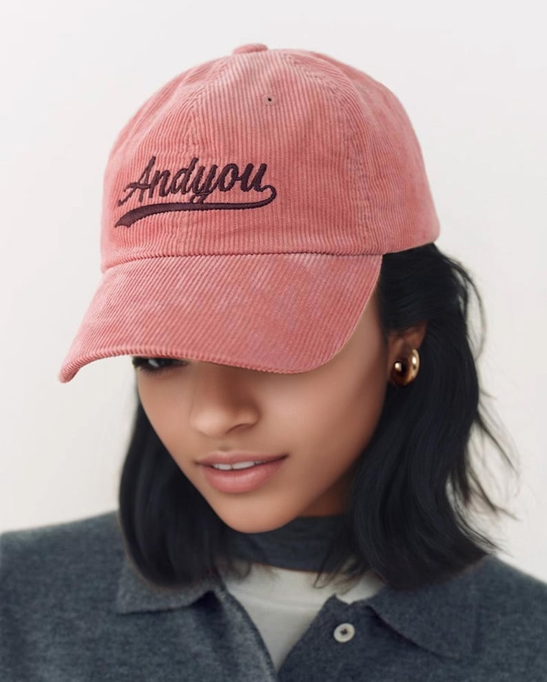 Puede incluir: Una gorra de b&eacute;isbol de pana rosa con el texto "Andy You" bordado en marr&oacute;n oscuro en la parte delantera.