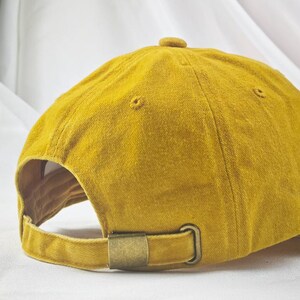 May include: A mustard yellow baseball cap with a brown metal buckle closure.