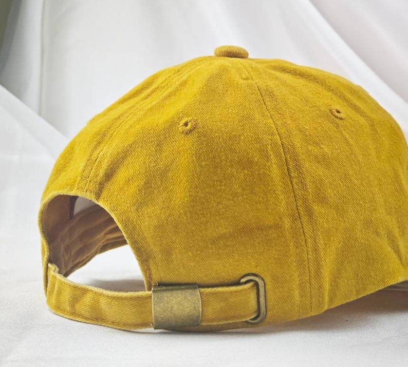 May include: A mustard yellow baseball cap with a brown metal buckle closure.