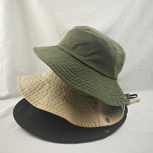 K&ouml;nnte beinhalten: Drei Bucket-Hats &uuml;bereinander gestapelt. Der oberste Hut ist gr&uuml;n, der mittlere Hut ist beige und der unterste Hut ist schwarz.