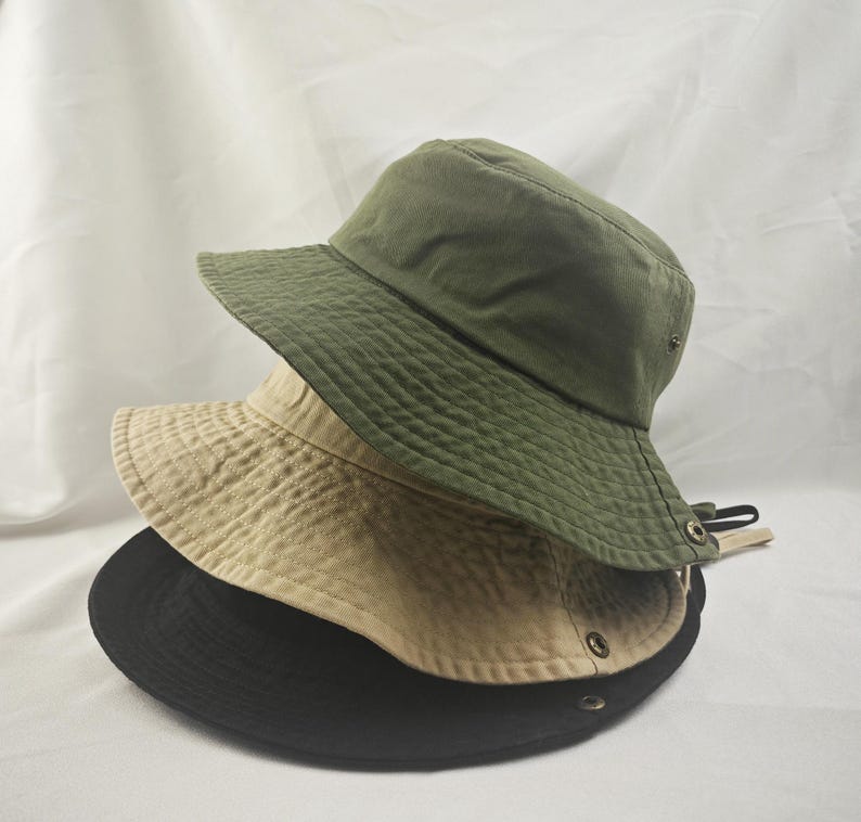 K&ouml;nnte beinhalten: Drei Bucket-Hats &uuml;bereinander gestapelt. Der oberste Hut ist gr&uuml;n, der mittlere Hut ist beige und der unterste Hut ist schwarz.