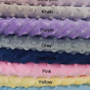 May include: Stack of eight fabric swatches in different colors, including coral pink, khaki, purple, gray, dark blue, pink, yellow, and baby blue. Each swatch has a textured surface with small raised dots.