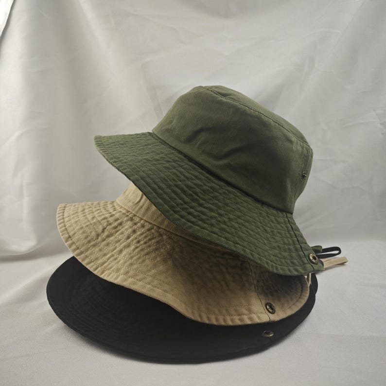 May include: Three bucket hats stacked on top of each other. The top hat is green, the middle hat is beige, and the bottom hat is black.