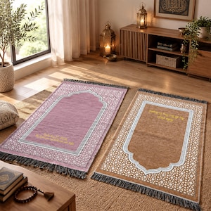 Op de afbeelding: Twee rechthoekige gebedskleden met franjes, één in mauve en één in bruin. Beide hebben een centraal mihrab-boogontwerp met ingewikkelde geometrische patronen langs de randen en goudkleurige geborduurde tekst in het midden.